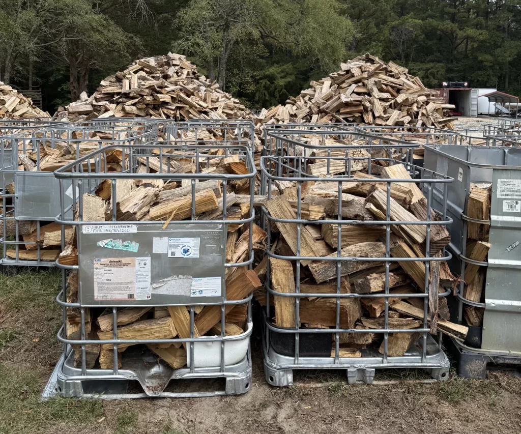 Fonvilletreeservice split firewood logs stacked in metal IBC tote cages at outdoor wood processing yard in NC