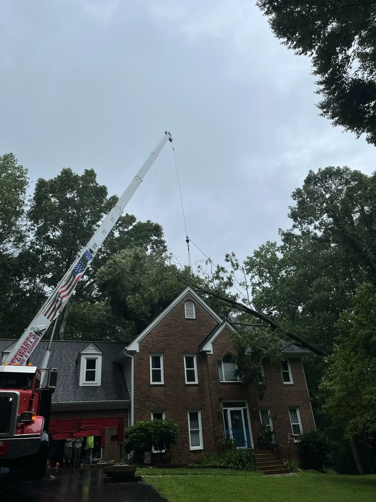 Crane lifting over a brick home during tree removal