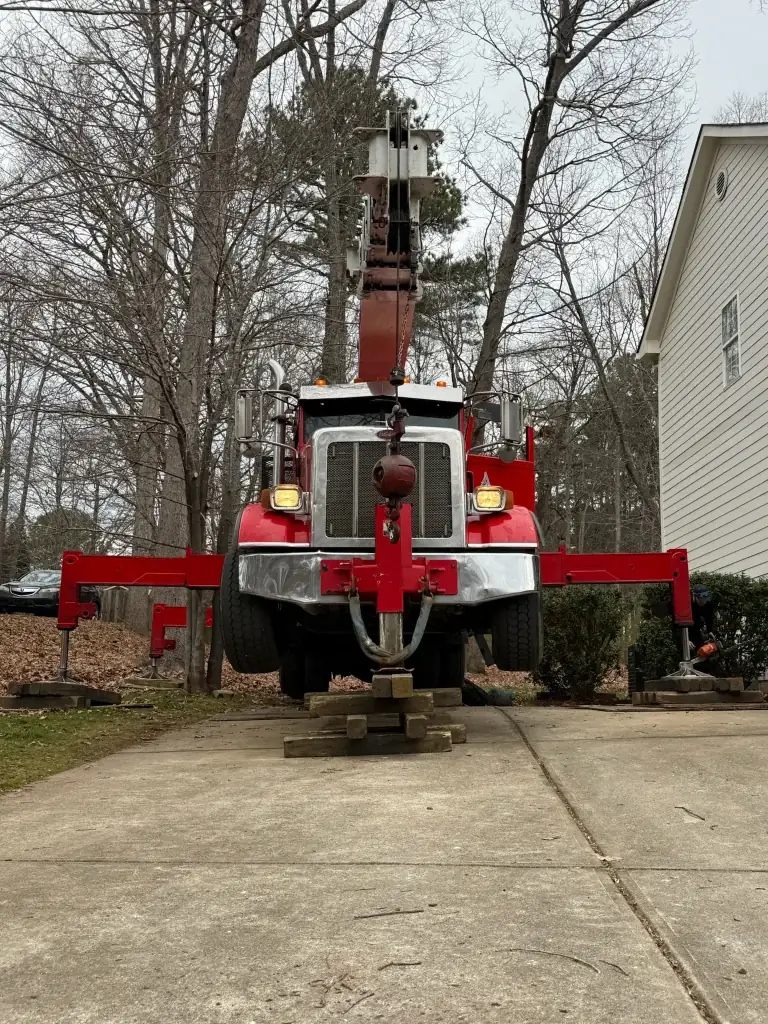 Fonvilletreeservice red crane truck with outriggers deployed and stabilized on wooden cribbing in residential driveway NC